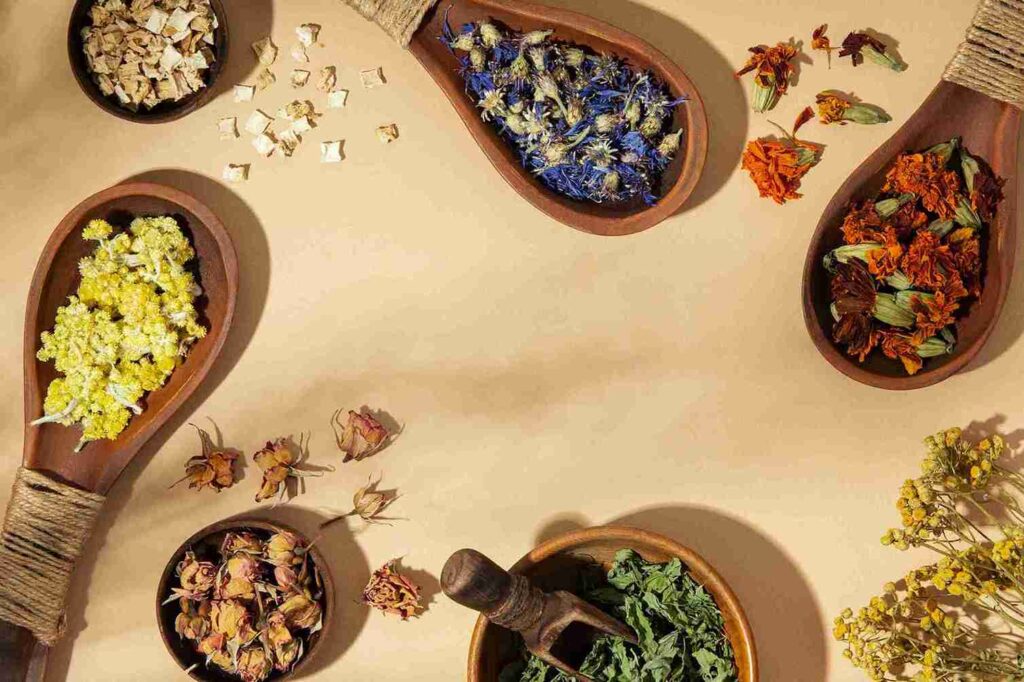 Berbagai bunga dan daun herbal kering di atas sendok kayu, menunjukkan bahan alami herbal untuk kulit