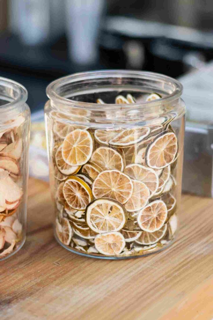 Sebuah stoples kaca bening yang diisi penuh dengan irisan jeruk nipis kering, tambahan yang menyegarkan untuk resep trail mix, diletakkan di atas permukaan kayu.