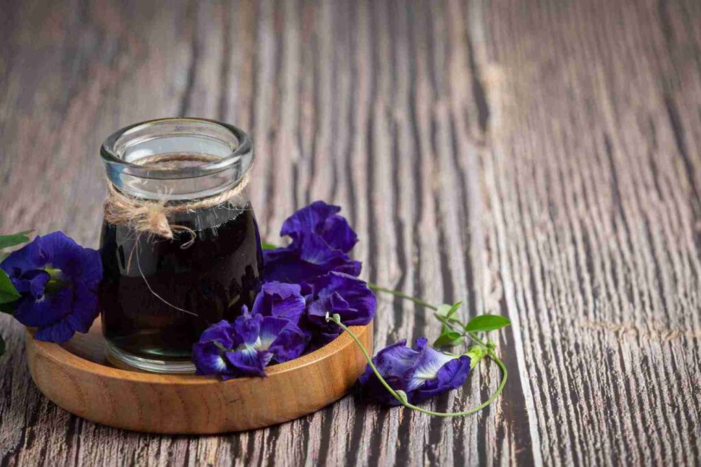 segelas minuman diatas meja kayu cantik dengan hiasan bunga telang yang menggambarkan manfaat bunga telang