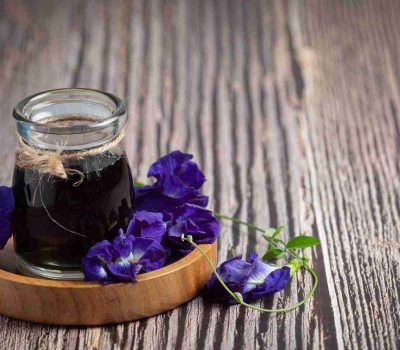 segelas minuman diatas meja kayu cantik dengan hiasan bunga telang yang menggambarkan manfaat bunga telang