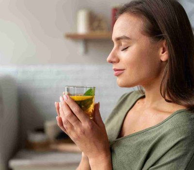 Wanita dengan kulit sehat meminum teh, menggambarkan konsep perawatan menggunakan herbal untuk kulit dari dalam